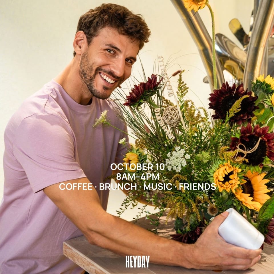 Smiling man arranges a colorful sunflower bouquet at a table during Heyday’s coffee, brunch, music, and friends event.