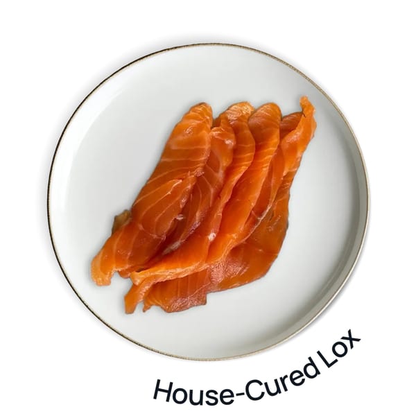 Slices of bright orange house-cured lox are fanned out on a white plate with a gold rim.