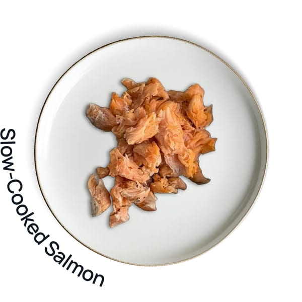 Flaked slow-cooked salmon on a white plate with a gold rim, viewed from above.