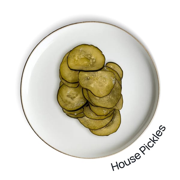 A white plate with a gold rim holds a pile of green, thinly sliced house pickles.