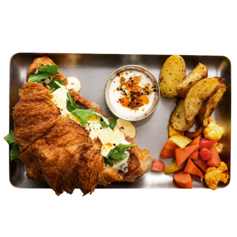 A croissant sandwich with arugula, cheese, and sauce, served with potato wedges, yogurt, and pickled vegetables.